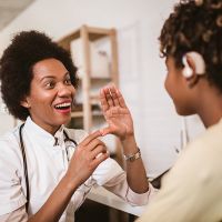 Black woman doctor with stethoscope, signing 'help' to another person